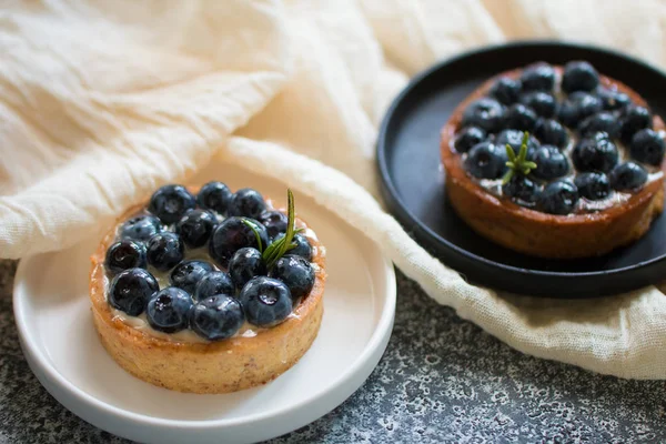 Gri arka plan üzerinde siyah ve beyaz tabaklar üzerinde vanilyalı muhallebi krema ile Lezzetli yaban mersini tartlets. Üstte görüntü. 