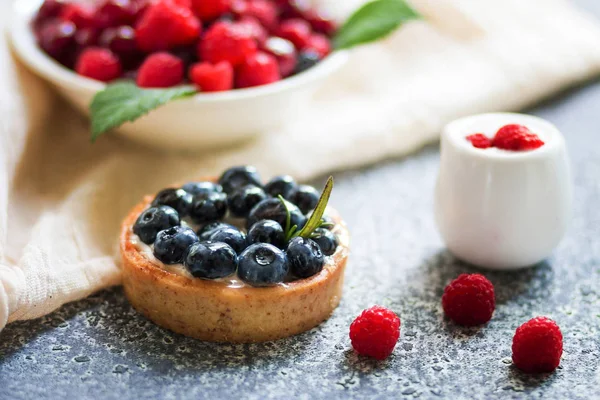 Yaban mersini ile Tartalet, taze ahududu ve gri yüzeyde ekşi krema ile süt ile plaka. 