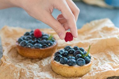 Bir kadının eli taze ahududu meyveleri ile nane kağıt üzerinde yatan tartalet süsler. 