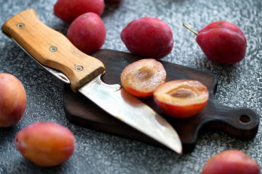 Bütün ve dilimlenmiş olgun erik, gri bir masa üzerinde ahşap bir tahta üzerinde ahşap saplı bir bıçak... Pastanın hazırlanması. Ön görünüm