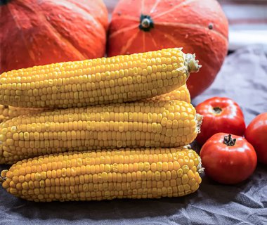 Arka planda haşlanmış mısır, gri keten peçete ve balkabağı domatesleri.