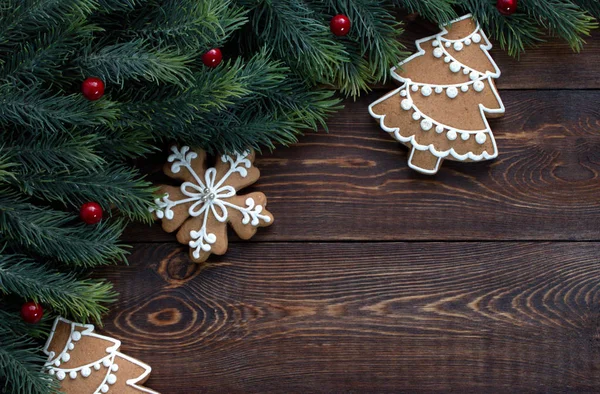 Quadro feito de ramos de abeto e pães de gengibre de Natal, bagas vermelhas, em uma superfície marrom de madeira . — Fotografia de Stock