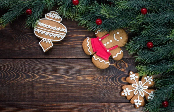 Quadro feito de ramos de abeto e pães de gengibre de Natal, bagas vermelhas, em uma superfície marrom de madeira . — Fotografia de Stock