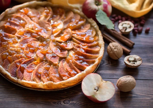 Apfelkuchen mit gerösteten Erdnüssen, Zimtstangen, frischem Apfel und Karamellsoße auf einem Teller auf dunkler Holzoberfläche — Stockfoto