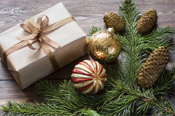 Vánoční složení zlatých vánočních míčků, dárek, smrkové větve na dřevěném hnědém povrchu. — Stock fotografie