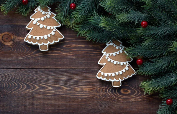 Rámeček z jedlových větví a vánočních perníčků, červené bobule, na dřevěném hnědém povrchu. — Stock fotografie