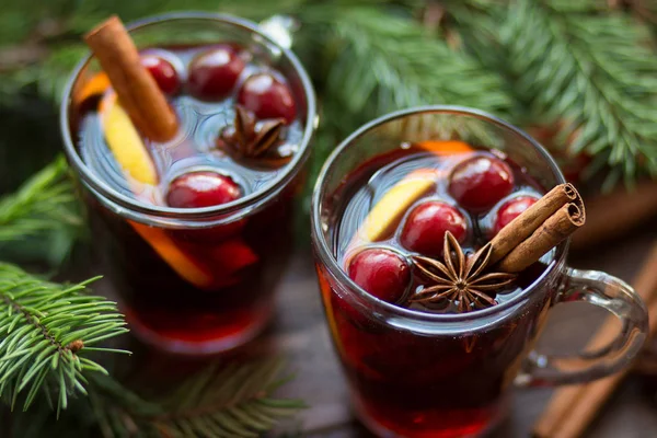 Mulled wine in glass mug with berries, cinnamon sticks and star anise on brown wood table