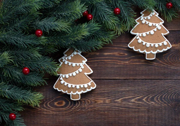 Quadro feito de ramos de abeto e pães de gengibre de Natal, bagas vermelhas, em uma superfície marrom de madeira . — Fotografia de Stock