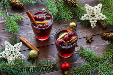 Böğürtlenli cam bardaklarda sıcak şarap, tarçın çubukları, yıldız anason ve kahverengi ahşap masada Noel oyuncakları..