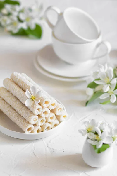 Dolci biscotti delicati sotto forma di tubi in scaglie di cocco ripieni di crema alla vaniglia su un piatto bianco — Foto Stock