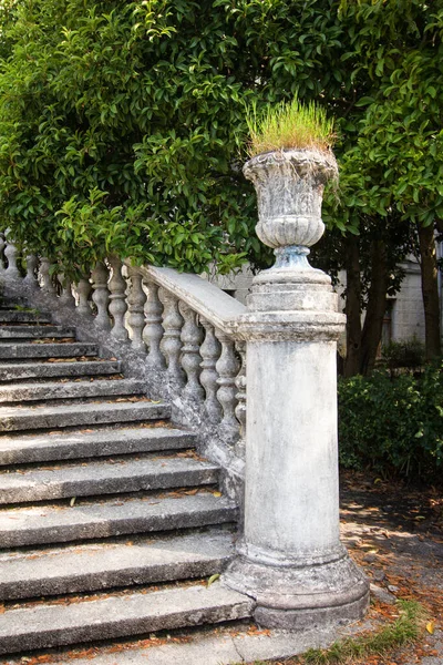 Stenen pot als decoratief element van een oude trap met stenen balusters op een achtergrond van groene vegetatie Stockfoto