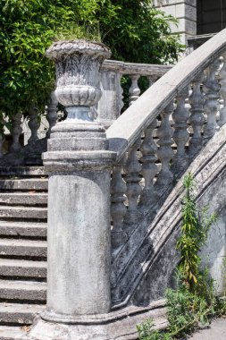 Taş kap, yeşil bitki örtüsünün arka planında taş balyaları olan antik bir merdivenin dekoratif bir elementi.