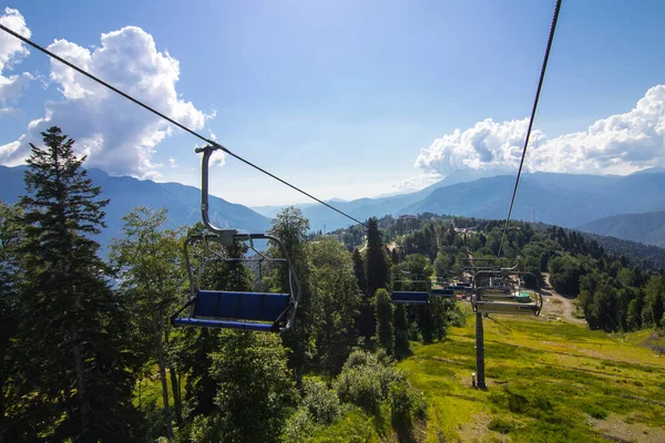 Cable car above mountain forest on a sunny Summer day. Green forests, hills, grassy meadows and blue sky. Summer holidays in the mountains.