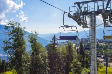 Güneşli bir yaz gününde Dağ Ormanı 'nın yukarısında teleferik. Yeşil ormanlar, tepeler, çimenli çayırlar ve mavi gökyüzü. Yaz tatili dağlarda.