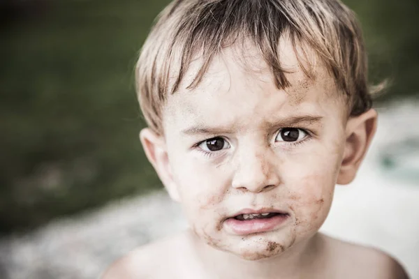 A little boy with a dirty face looking sad.