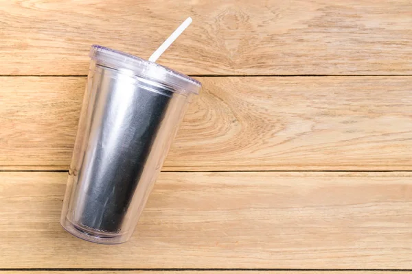 Top view plastic tumbler cup with straw or tube on wooden backgr