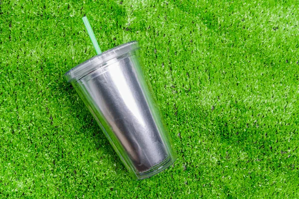 Top view plastic tumbler cup with straw or tube on Green grass