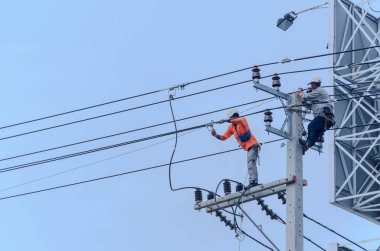 Elektrikçiler elektrik hatlarını kurmak ve onarmak için elektrik direklerine tırmanıyorlar..