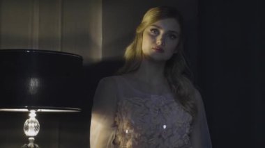 nazik zarif dantelli elbise standları antika masa lambası loş odada, ağır çekim güzel sarışın uzun saçlı kız