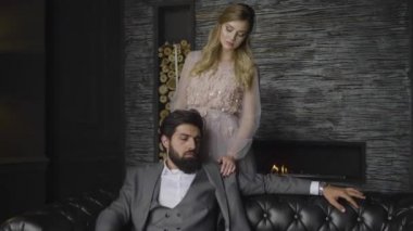 duvar, omuzlarına ellerini koyarak arka tarafından ağır çekim yakışıklı sakallı adam gri elbiseli kanepe sarışın Bayan üzerinde oturur standları