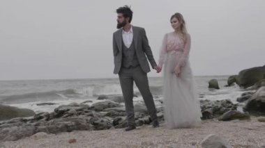 ağır çekim şiddetli sakallı adam müşteri adayları ihale kız güzel içinde uzun bir elbise kayalık plaj elle gri deniz sallayarak tarafından