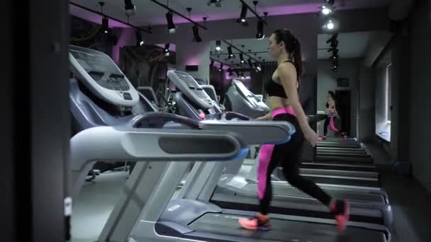 在体育俱乐部里 穿着黑色上衣和粉色运动鞋的漂亮黑发女人在跑步机上快速行走 — 图库视频影像