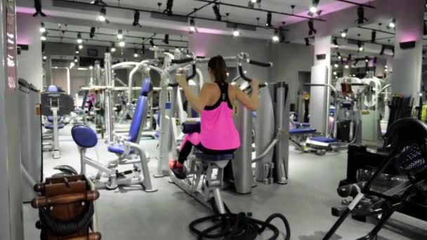 鼓舞人心的背面视图女孩在粉红色的黑色上衣和紧身裤做运动在高 Lat 下拉在现代健身房 — 图库视频影像