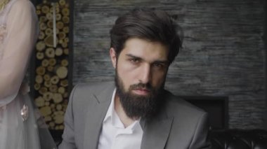 ağır çekim portre yakışıklı şiddetli adamla kalın sakal ve hüzünlü gözleri kamera dekore edilmiş duvara bakarak oturur