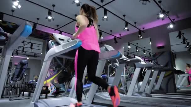 令人兴奋的女士在紫色的黑色上衣和紧身裤停止运行在灰色跑步机上的体育俱乐部背面视图 — 图库视频影像