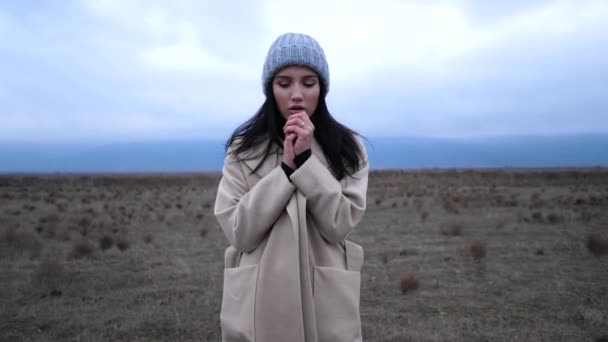 Woman in coat breathes on hands in cold morning slow motion — ストック動画
