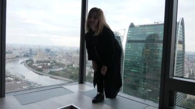 Büyük Fransız pencereleri resimsel şehir manzaralı, uzun siyah hırka genç güzel sarışın kadın ayağa kalkar