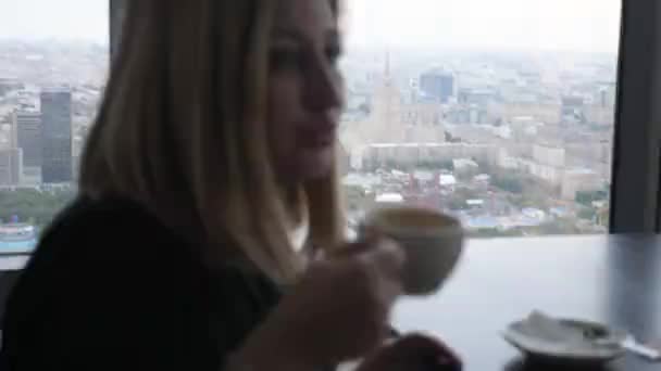 鼓舞人心的近距离的看法美丽的女士喝咖啡和微笑坐在与城市全景的窗口 — 图库视频影像