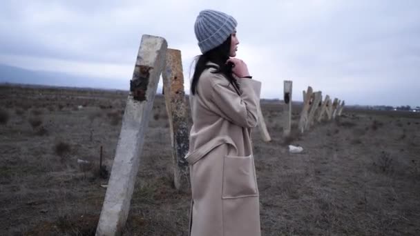 Kobieta w swobodnym ubraniu stoi w pobliżu starych biegunów na polu powoli — Wideo stockowe