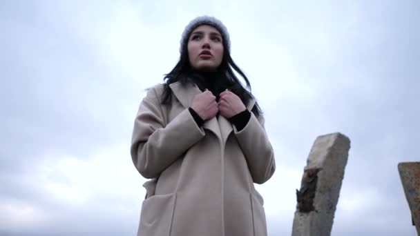 Girl wraps in spring coat against cloudy sky slow motion — Stock Video