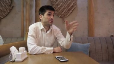 yakışıklı koyu saçlı adam komik jest ile garson modern kafede ayna yakınında ahşap masada oturan çağırır