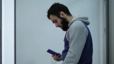 kapüşonlu sakallı kişi beyaz duvarları ile odada yürüyor
