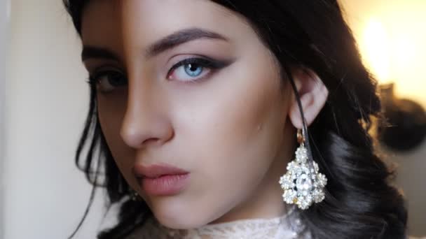 Mooie jonge dame met oorbellen en make-up kijkt naar de camera — Stockvideo