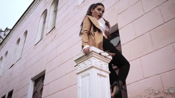 Beautiful girl sits by white building with sunglasses — Stock Video