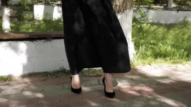Büyük cepleri ve siyah topuklu ayakkabıları olan uzun siyah etekli bir kadın.