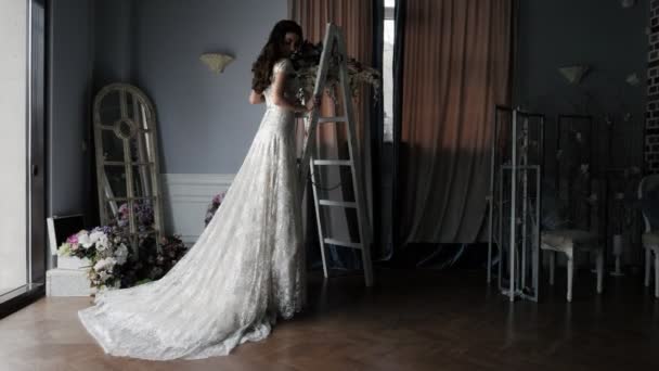 Невеста с длинными каштановыми волосами стоит у лестницы в кружевном платье — стоковое видео