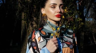 dolgun kırmızı dudakları ve el yapımı uzun küpe ile şık genç bayan bahar dal closeup yavaş hareket tutarak duruyor