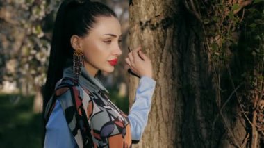 parlak modern elbise at kuyruğu kırmızı dudaklar ve uzun küpe ile muhteşem genç kız ağaç gövdesi yavaş hareket duruyor