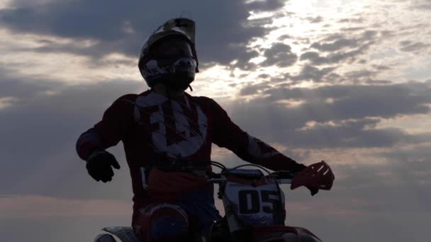 Racer in helm silhouet verhoogt de handen onder bewolkte hemel — Stockvideo