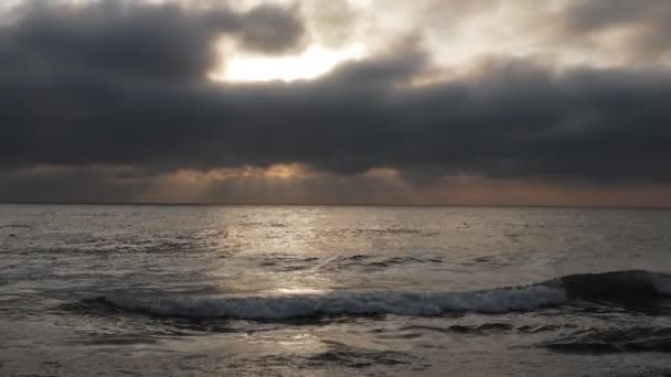 無限の海の波が海岸線に転がり 灰色の密集した雲の後ろから夕方の太陽光を反射する — ストック動画