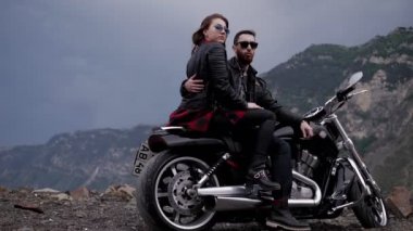 heyecanlı sevgi dolu çift sarılıyor ve akşamları dağlara karşı modern motosiklet üzerinde oturuyor