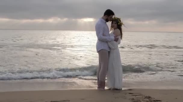 女人在长白色夏装固定头发 而站在英俊的男朋友手臂在沙滩上 — 图库视频影像