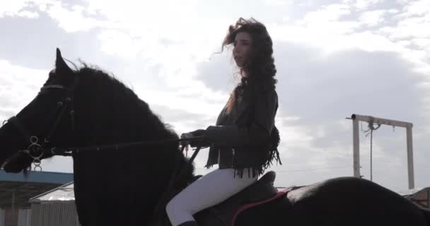 Νεαρή όμορφη γυναίκα σε δερμάτινο μπουφάν βόλτες μαύρο άλογο — Αρχείο Βίντεο
