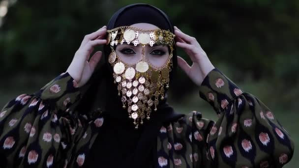 Lady in hijab and golden coin face veil holds hands at head — Stock Video