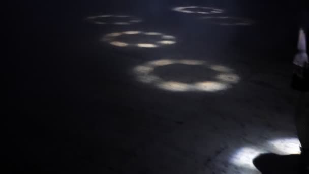 Леді в чорному стоїть на підлозі з кружляючими світловими колами — стокове відео