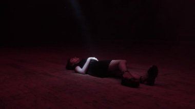 siyah elbise ve file tayt zarif bayan geniş karanlık sahnede parlak ışık kiriş altında yatıyor 